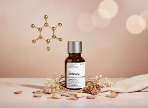 Close-up product photograph of a 30ml The Ordinary Hyaluronic Acid 2% + B5 serum in a dark amber glass dropper bottle with silver cap, centered on a soft beige fabric with scattered dried rose petals, eucalyptus leaves, and dried flowers in a nest-like arrangement; a large metallic molecular structure model glows in golden bokeh lights on the upper left, evoking luxury skincare elegance.