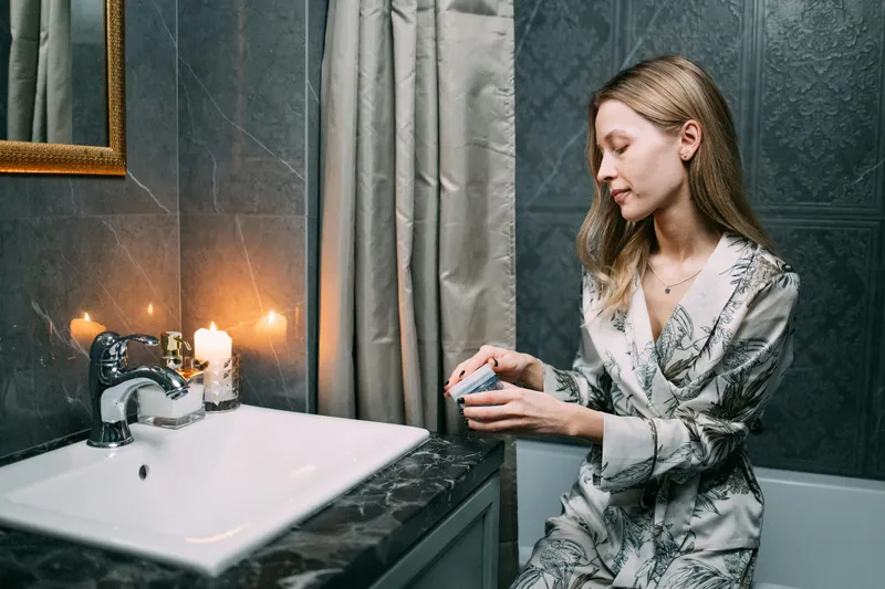Relaxed woman in cozy pajamas applying skincare product with minimal bathroom counter setup