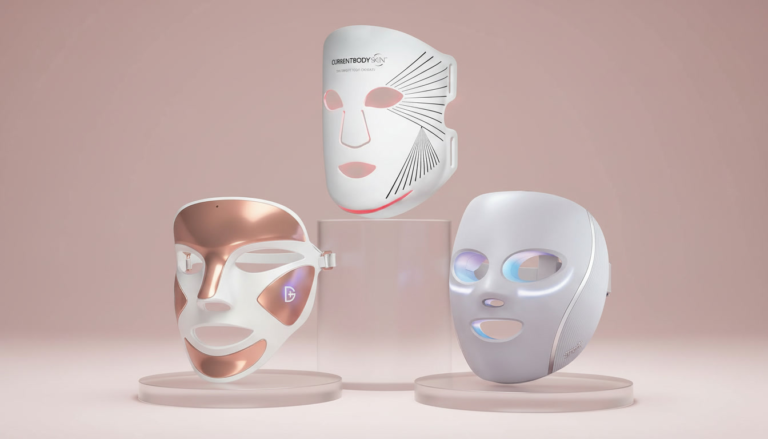 Three top-rated red light therapy masks for 2026 displayed at varying heights on frosted glass pedestals against a blush pink backdrop